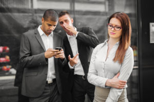 Male colleagues whispering gossip about their new female colleague.